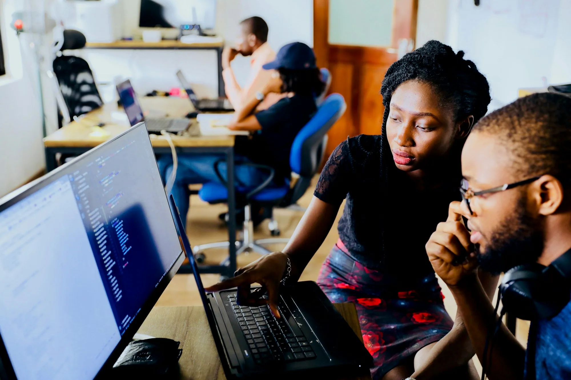 Two developers reviewing an AI automation workflow on a laptop in a busy office